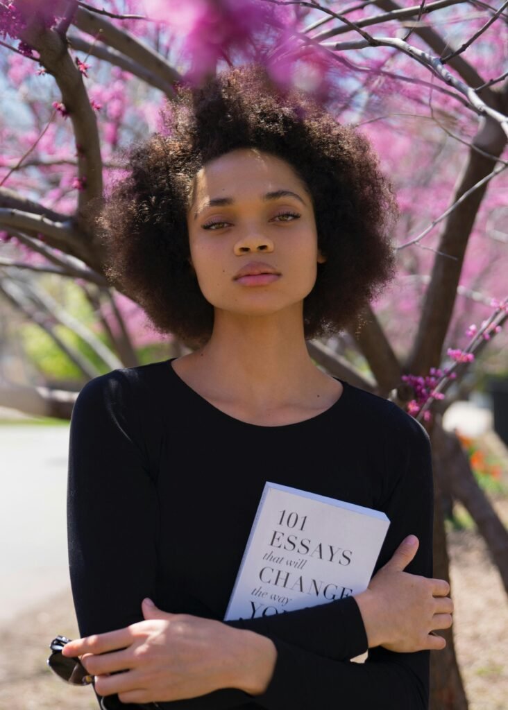 pexels-photo-2228560-2228560 Portrait of an African American woman embracing a book among spring blossoms.